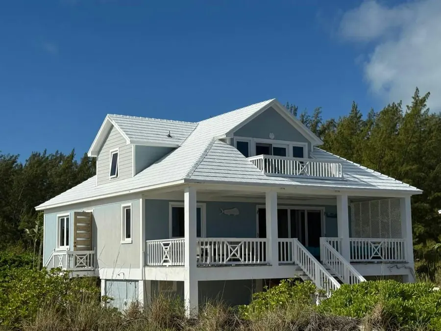 Pale blue coastal beach house with white railings and a covered porch under a clear sky